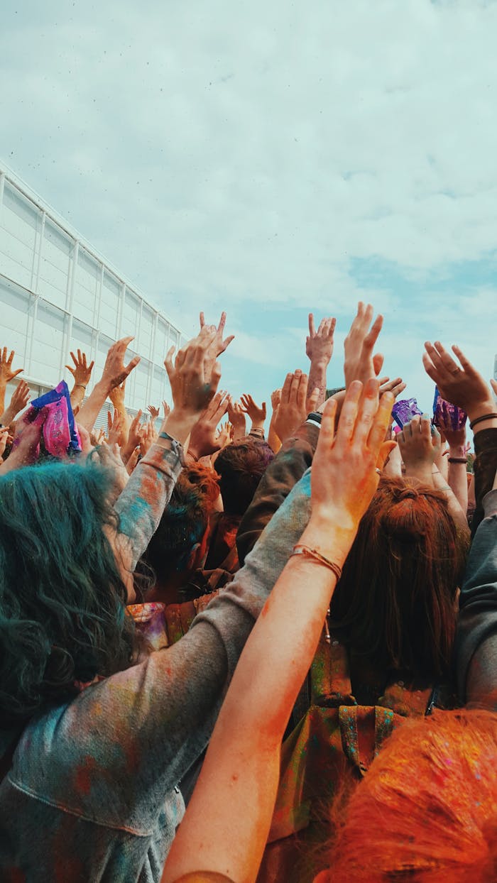 Crowd of people with colorful powder on hands raising them in joy during an outdoor celebration.